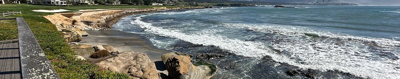Rocky coastline with waves crashing against the shore under a cloudy sky.