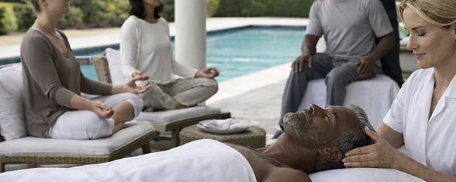 A man relaxes by a pool with two people meditating nearby.
