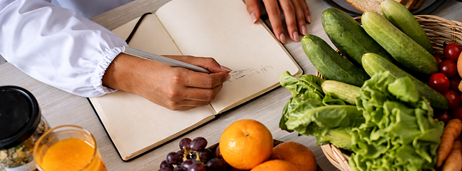 Person sketching a fruit bowl in a notebook beside fresh produce.